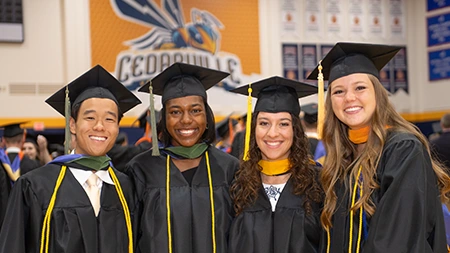Four students in graduation regalia smiling in gym