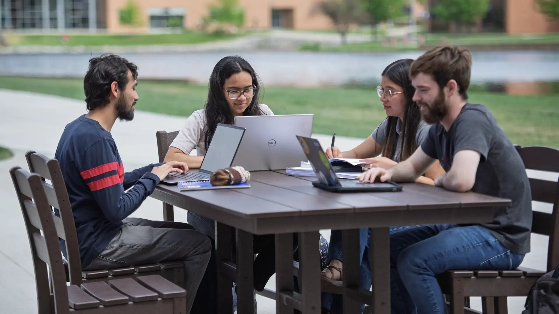students studying table outdoors Four students sitting around a patio table with open laptops.