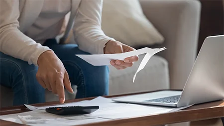 Person reviewing financial documents and using a calculator to manage education expenses.