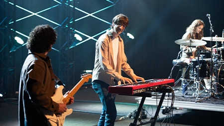 Students playing keyboard, guitar, and drums onstage in chapel