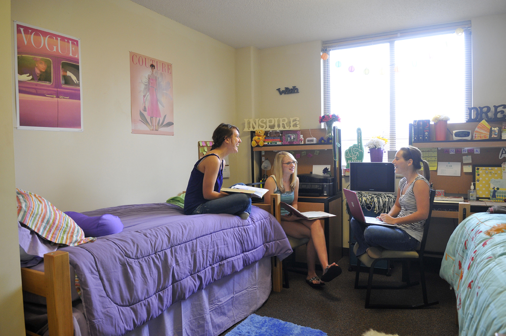 Three girls hanging out in a dorm room.