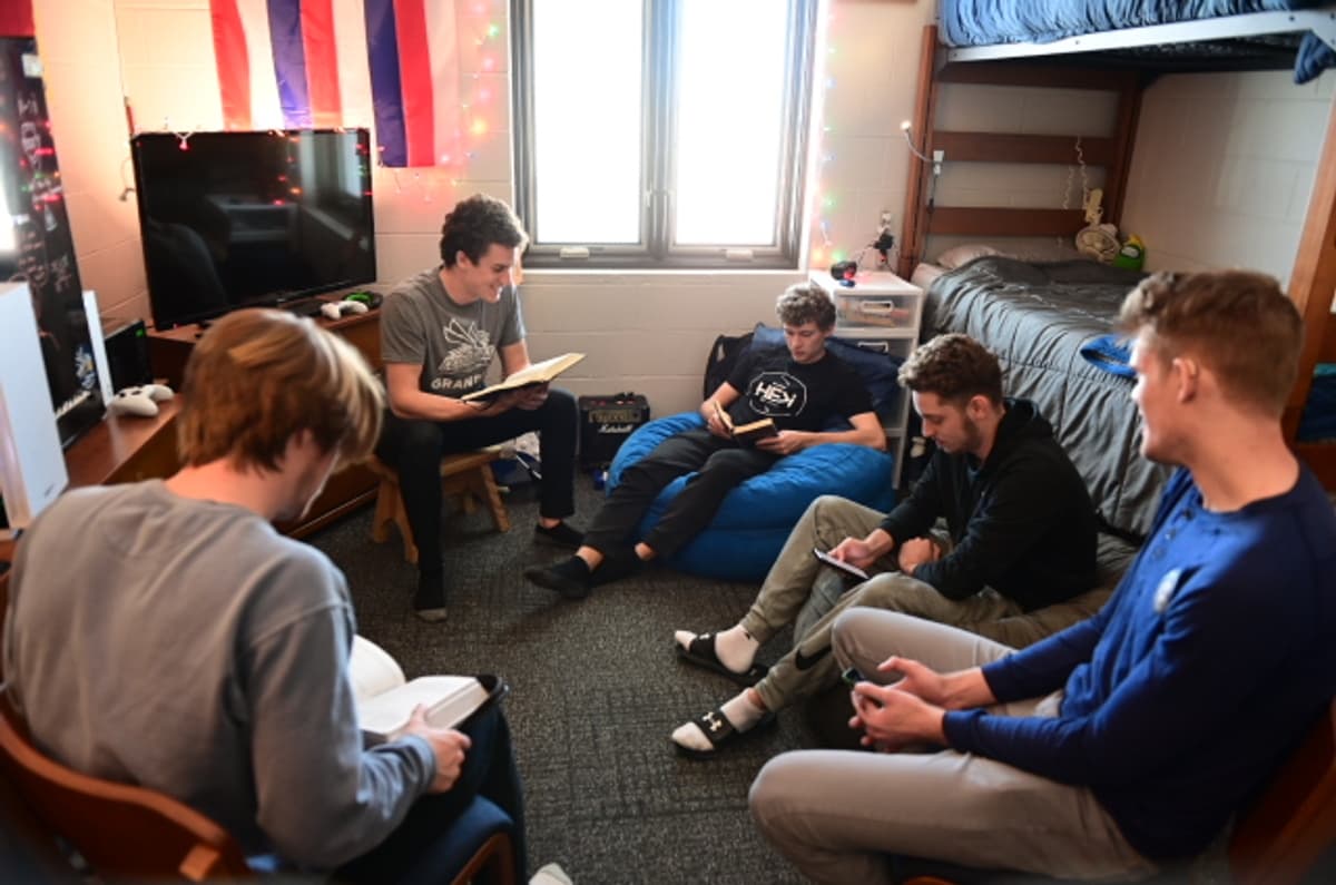 five male students read their Bibles together in a dorm room.