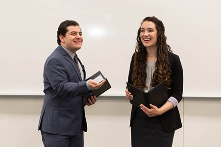 Two college students giving a speech holding notepads