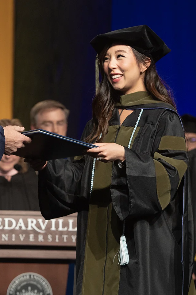 Graduate student in graduation regalia receiving diploma