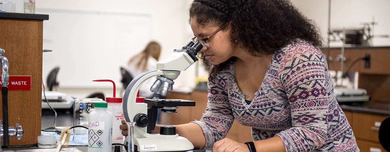 Female forensic science student looks through microscope