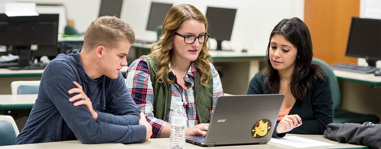 Three students discuss around a laptop