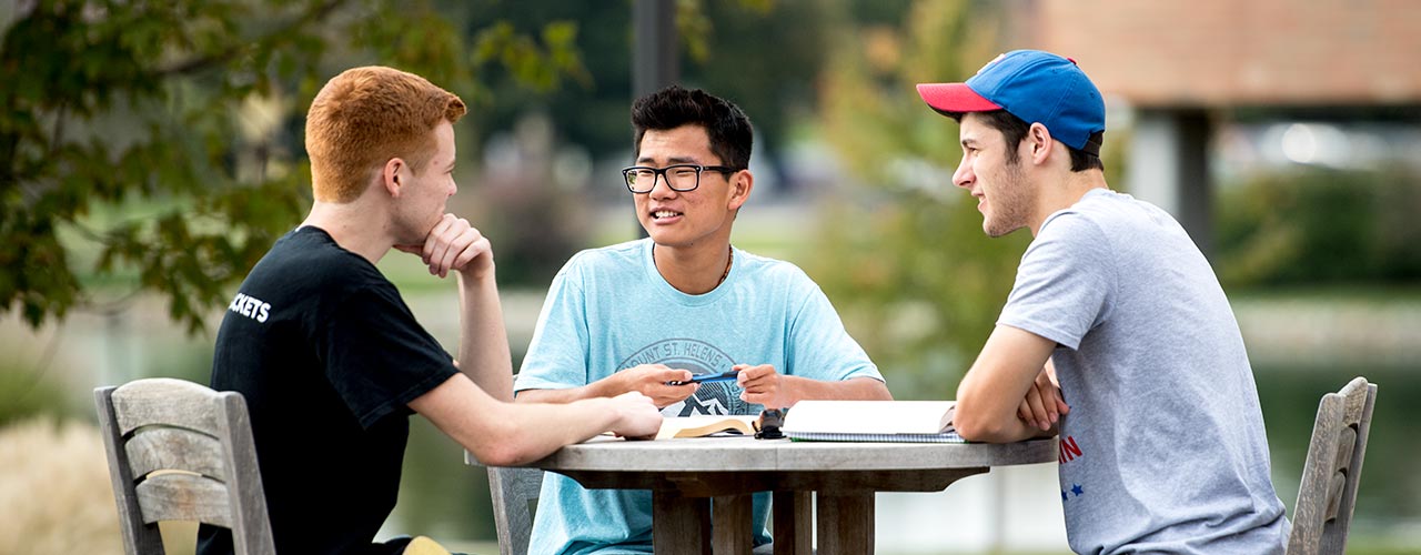 Three male students do homework at a patio table