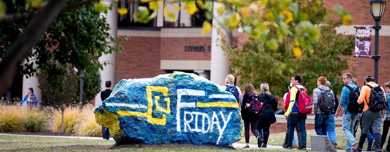 Students walk past the rock painted with CU Friday