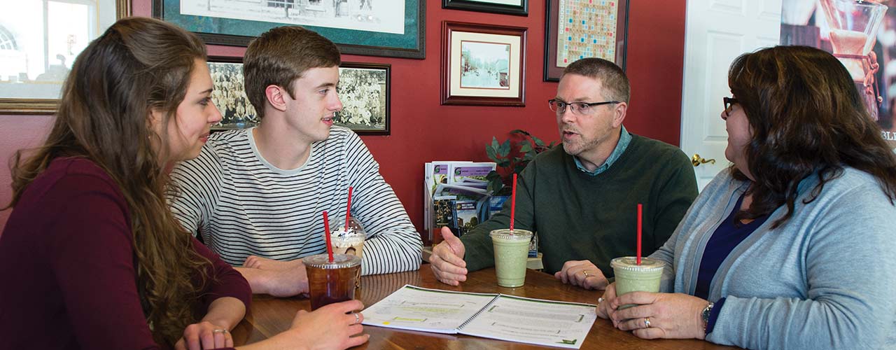Two engaged students discuss with a faculty mentor couple in a coffee shop