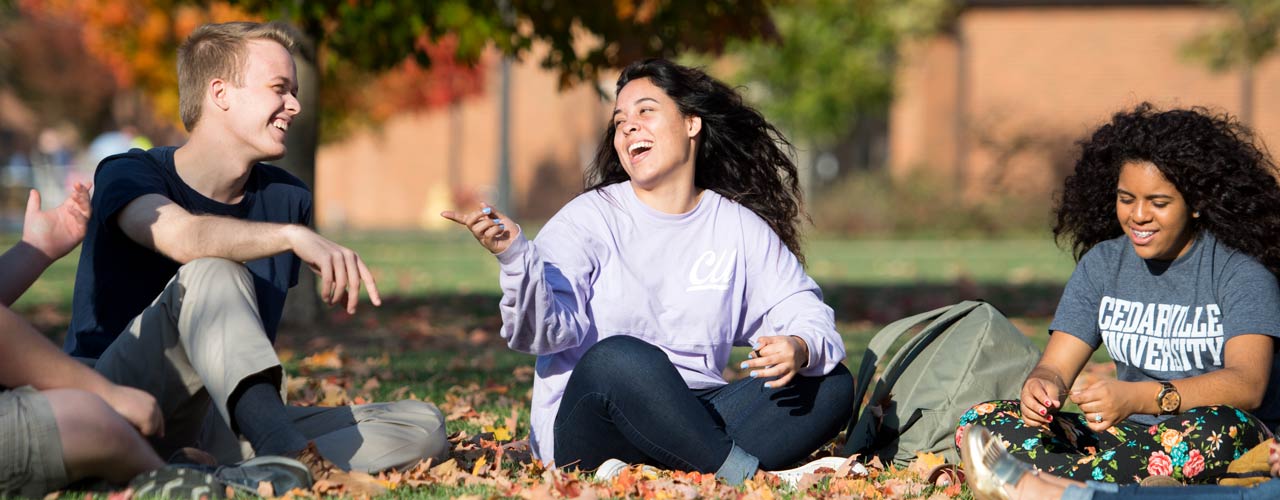 A group of diverse Cedarville students laugh among fall leaves