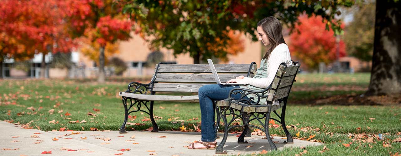 Female student sits on a bench on campus