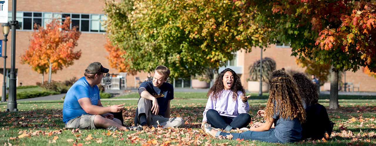 Group of Cedarville students relax in the grass and autumn leaves