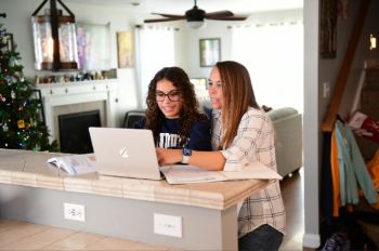 A homeschool student and her mother look at a computer together.