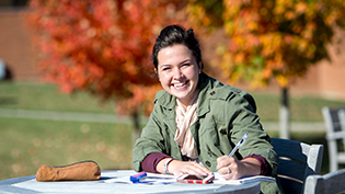 A female student does homework outside in the fall