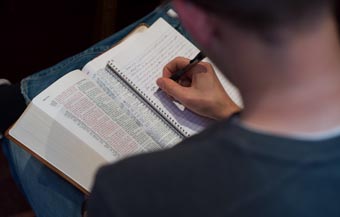 A student studying the Bible and writing notes in a notebook.