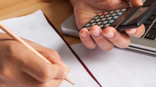 White hands holding a pencil and a calculator over paper on a desk