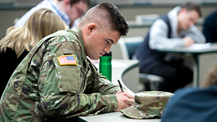 Man in army uniform taking notes in class.