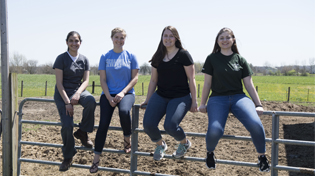 Four female students sitting on a cattle gate smiling at the camera