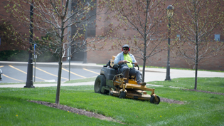 A student worker mowing the grass on campus