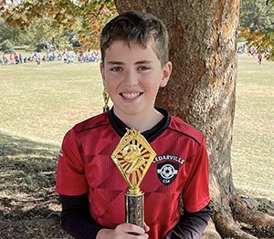 Boy holding a trophy under a shade tree.