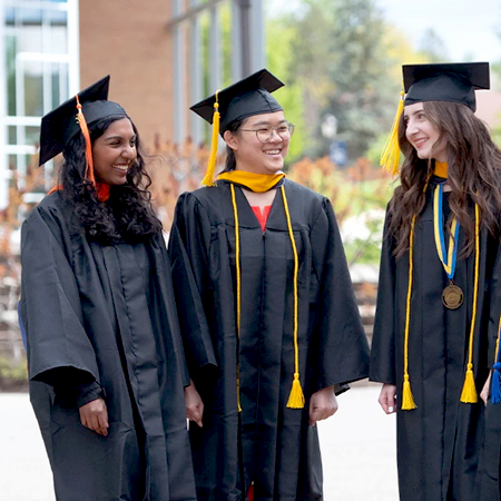 Three college students smiling in graduation regalia.