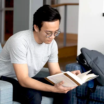 Male college student sitting in chair reading textbook