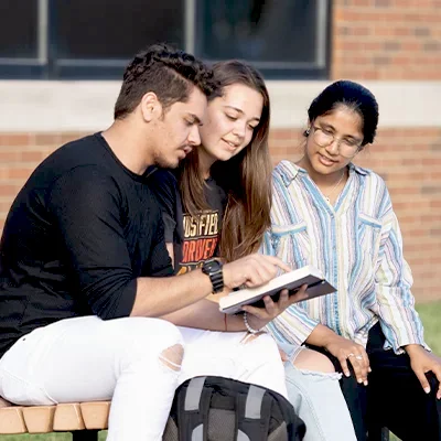 Three college students sitting on bench outside reading Bible