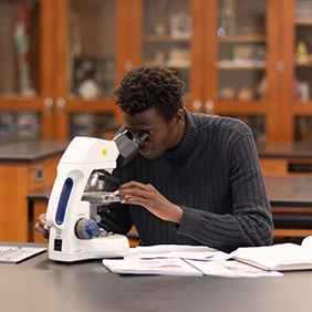 Male college student sitting at lab table looking through microscope