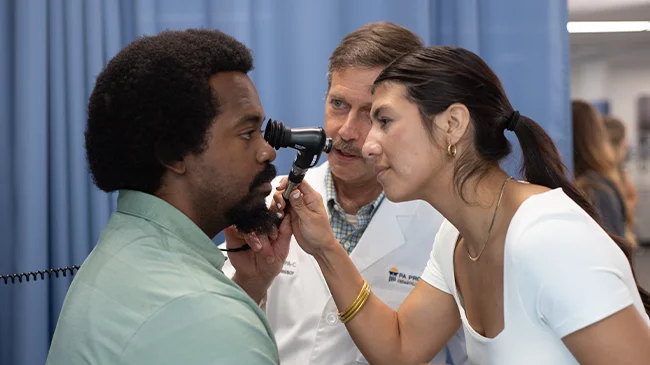 Professor looks on as physician assistant student examines the eye of another student
