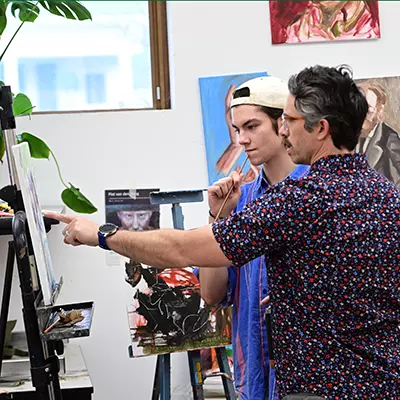 Student and professor at an easel reviewing the student's painting.