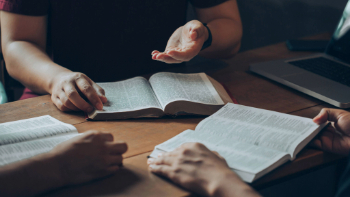 Three people sit with their open Bibles on a wooden table.
