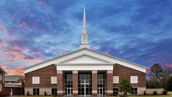 A brick church with a white steeple and cross stands out against the evening sky.