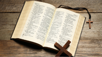 An open Bible with a cross resting on it is laying on a wooden table