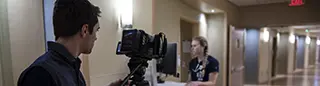Guy using professional video camera to record a health worker working in a hospital