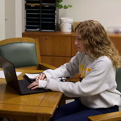 Female student seated at a table working on a laptop computer.