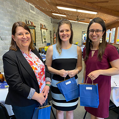 Three female alumni standing with gift bags