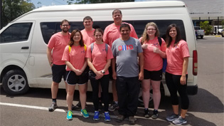 A group pf faculty and students in front of a van wearing  matching shirts