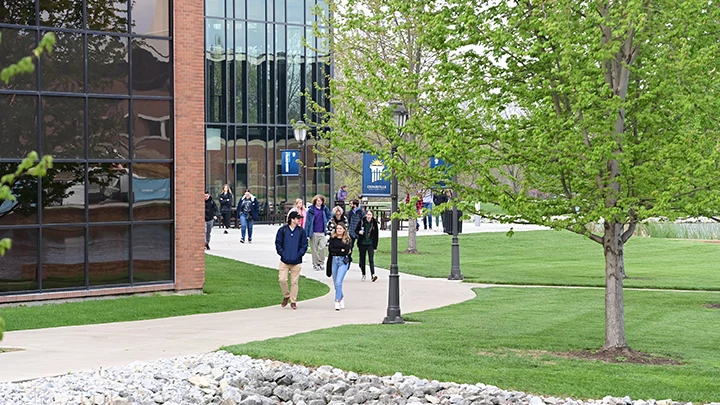 Students walking on campus by a glass and brick building in the summer.