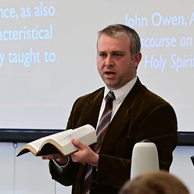 Bible professor holding an open Bible and teaching students
