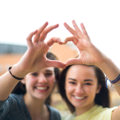 Two female students make a heart with their hands