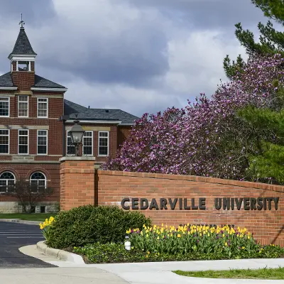 Founders' hall in springtime with flowers and the Cedarville University brick sign in front of it