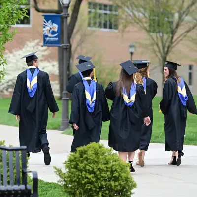 Students in graduation gowns talking and walking down the sidewalk