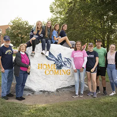 Family sitting on and standing by the rock during homecoming