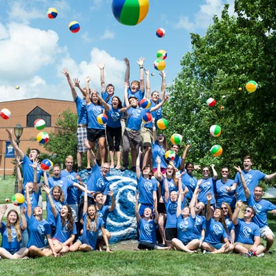 picture of students celebrating on the Cedarville rock while wearing cove shirts and tossing beach balls in the air