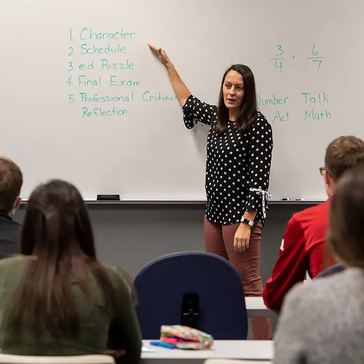 Woman standing at a whiteboard in front of seated students.