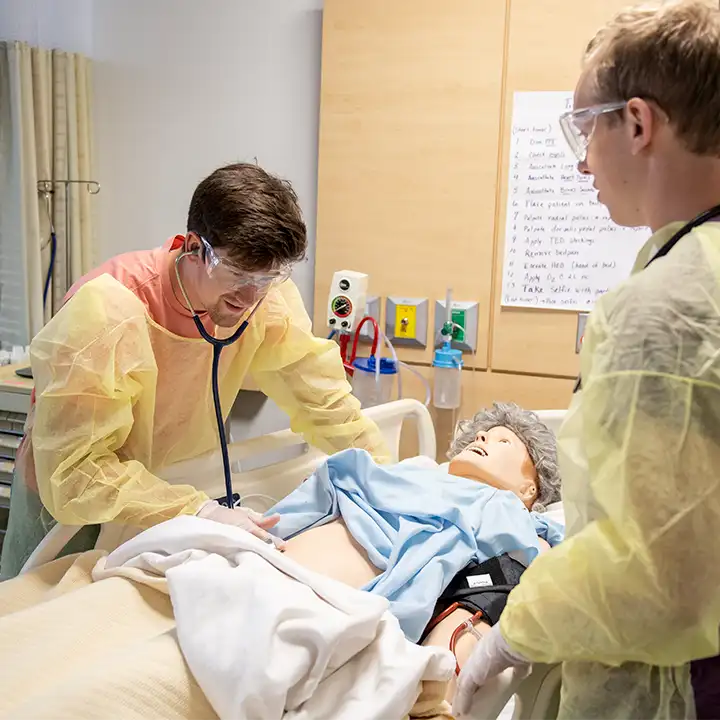 Two people in medical gowns working on a mannequin