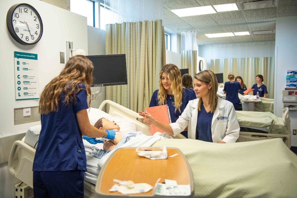 Student nurses training in a hospital setting bedside with a mannequin patient.