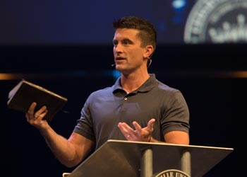 A man speaks on a large stage holding a Bible.