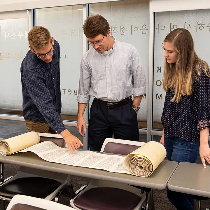 Three people standing over an open scroll