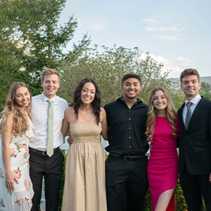 Group of students smiling in formal clothes outside.